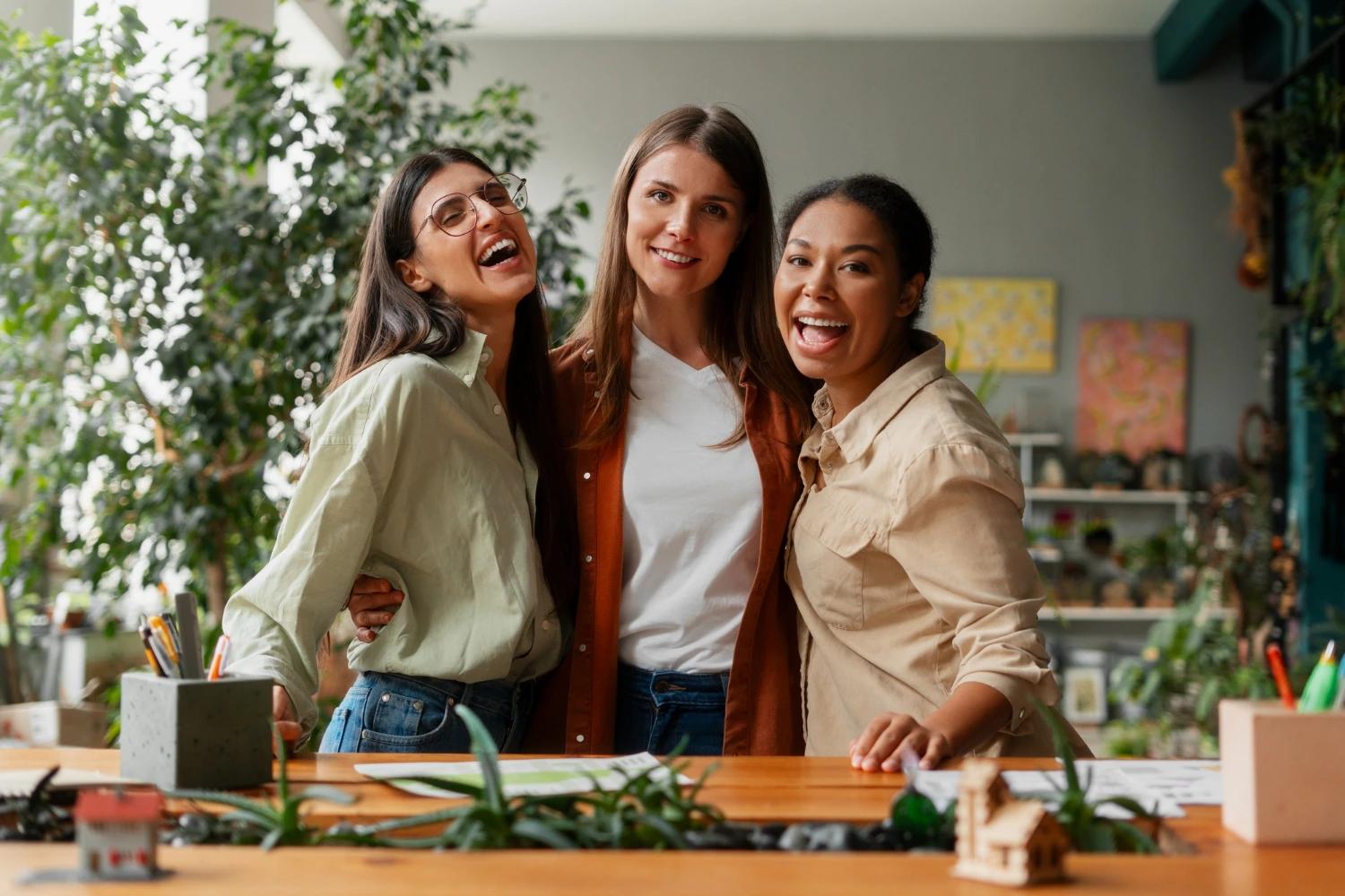 Três mulheres sorridentes em um ambiente de trabalho colaborativo e sustentável, representando união e diversidade entre mulheres no ESG.