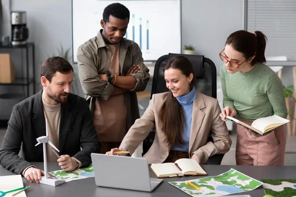 Grupo de profissionais discutindo projetos ambientais em um escritório, analisando mapas e gráficos ao redor de um laptop, representando colaboração e carreira sustentável na educação.
