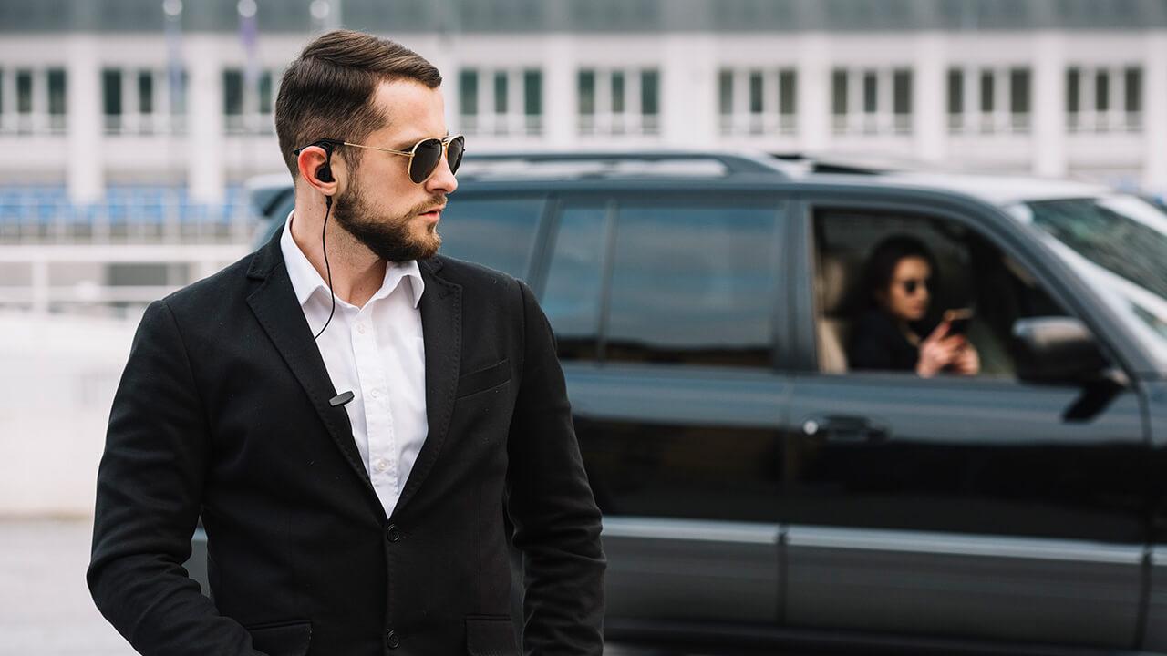 Homem vestido como um segurança de óculos escuros em frente a um carro.