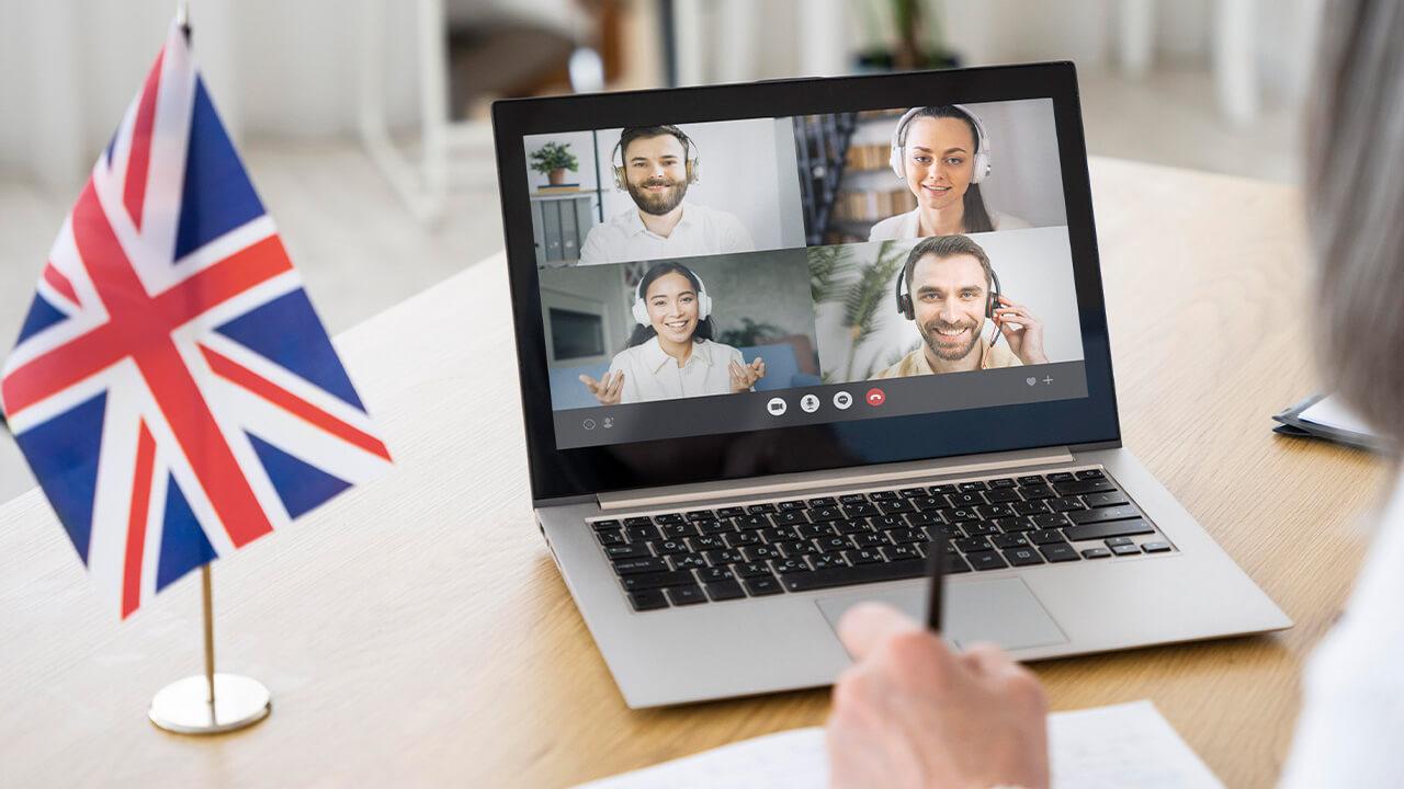 Pessoa fazendo videochamada com outras quatro pessoas e uma bandeira da Inglaterra ao lado, provavelmente falando em língua inglesa.